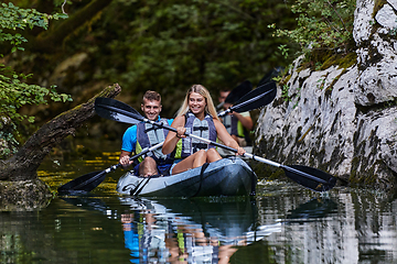 Image showing A group of friends enjoying having fun and kayaking while exploring the calm river, surrounding forest and large natural river canyons