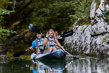 Image showing A group of friends enjoying having fun and kayaking while exploring the calm river, surrounding forest and large natural river canyons