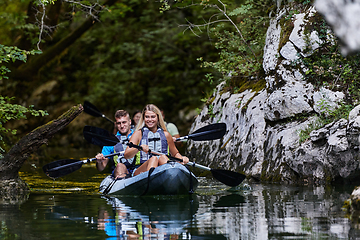 Image showing A group of friends enjoying having fun and kayaking while exploring the calm river, surrounding forest and large natural river canyons