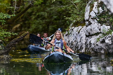 Image showing A group of friends enjoying having fun and kayaking while exploring the calm river, surrounding forest and large natural river canyons