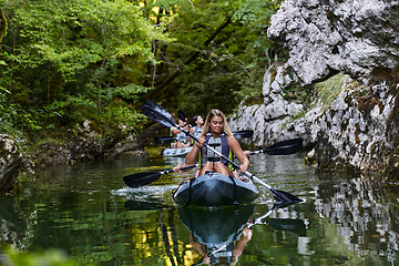 Image showing A group of friends enjoying having fun and kayaking while exploring the calm river, surrounding forest and large natural river canyons