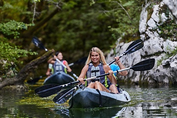 Image showing A group of friends enjoying having fun and kayaking while exploring the calm river, surrounding forest and large natural river canyons