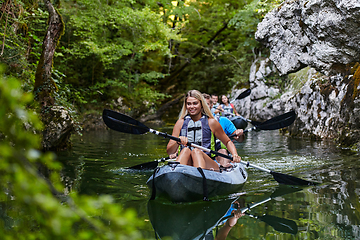 Image showing A group of friends enjoying having fun and kayaking while exploring the calm river, surrounding forest and large natural river canyons