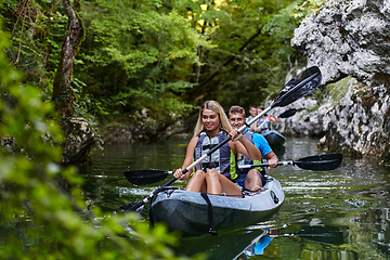 Image showing A group of friends enjoying having fun and kayaking while exploring the calm river, surrounding forest and large natural river canyons