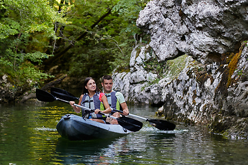 Image showing A young couple enjoying an idyllic kayak ride in the middle of a beautiful river surrounded by forest greenery