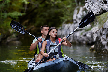 Image showing A young couple enjoying an idyllic kayak ride in the middle of a beautiful river surrounded by forest greenery