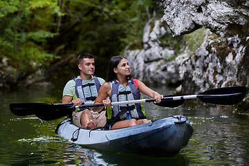 Image showing A young couple enjoying an idyllic kayak ride in the middle of a beautiful river surrounded by forest greenery