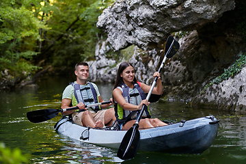 Image showing A young couple enjoying an idyllic kayak ride in the middle of a beautiful river surrounded by forest greenery