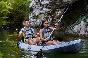 Image showing A young couple enjoying an idyllic kayak ride in the middle of a beautiful river surrounded by forest greenery