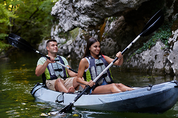 Image showing A young couple enjoying an idyllic kayak ride in the middle of a beautiful river surrounded by forest greenery