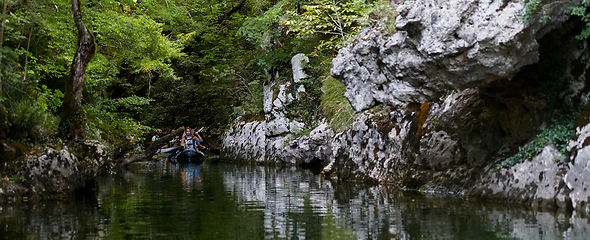 Image showing A group of friends enjoying having fun and kayaking while exploring the calm river, surrounding forest and large natural river canyons