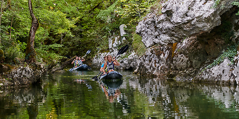 Image showing A group of friends enjoying having fun and kayaking while exploring the calm river, surrounding forest and large natural river canyons