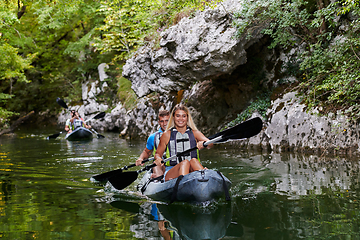 Image showing A group of friends enjoying having fun and kayaking while exploring the calm river, surrounding forest and large natural river canyons