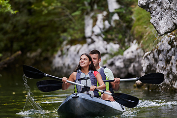 Image showing A young couple enjoying an idyllic kayak ride in the middle of a beautiful river surrounded by forest greenery