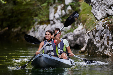 Image showing A young couple enjoying an idyllic kayak ride in the middle of a beautiful river surrounded by forest greenery