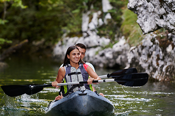 Image showing A young couple enjoying an idyllic kayak ride in the middle of a beautiful river surrounded by forest greenery