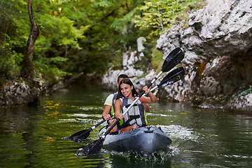 Image showing A young couple enjoying an idyllic kayak ride in the middle of a beautiful river surrounded by forest greenery