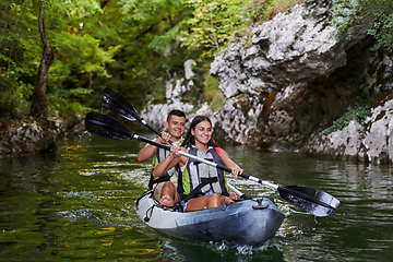 Image showing A young couple enjoying an idyllic kayak ride in the middle of a beautiful river surrounded by forest greenery