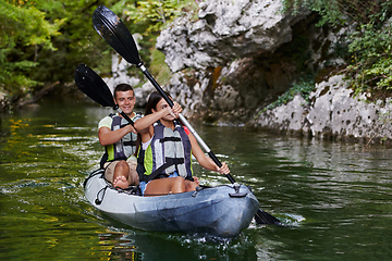 Image showing A young couple enjoying an idyllic kayak ride in the middle of a beautiful river surrounded by forest greenery