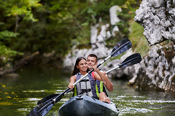 Image showing A young couple enjoying an idyllic kayak ride in the middle of a beautiful river surrounded by forest greenery