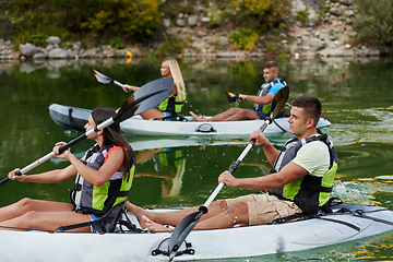 Image showing A group of friends enjoying having fun and kayaking while exploring the calm river, surrounding forest and large natural river canyons