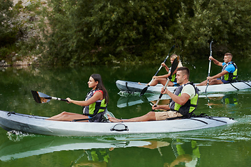 Image showing A group of friends enjoying having fun and kayaking while exploring the calm river, surrounding forest and large natural river canyons