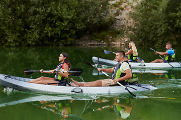 Image showing A group of friends enjoying having fun and kayaking while exploring the calm river, surrounding forest and large natural river canyons