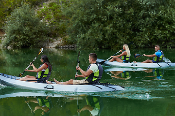 Image showing A group of friends enjoying having fun and kayaking while exploring the calm river, surrounding forest and large natural river canyons