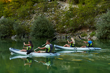 Image showing A group of friends enjoying having fun and kayaking while exploring the calm river, surrounding forest and large natural river canyons