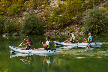 Image showing A group of friends enjoying having fun and kayaking while exploring the calm river, surrounding forest and large natural river canyons