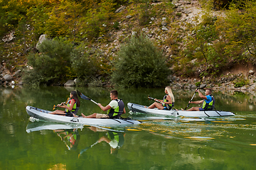 Image showing A group of friends enjoying having fun and kayaking while exploring the calm river, surrounding forest and large natural river canyons