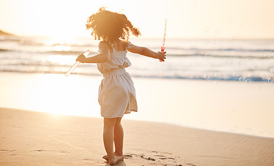 Image showing Girl child, bubbles and back by beach in sunset, playing and freedom by waves, games and ocean vacation. Young female kid, plastic toys and soap with water in summer sunshine by sea for holiday