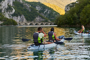 Image showing A group of friends enjoying having fun and kayaking while exploring the calm river, surrounding forest and large natural river canyons