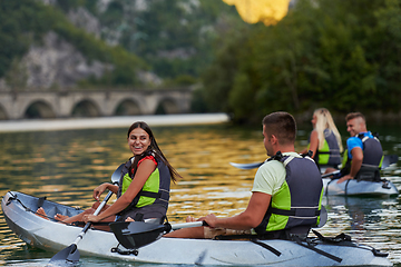 Image showing A group of friends enjoying having fun and kayaking while exploring the calm river, surrounding forest and large natural river canyons