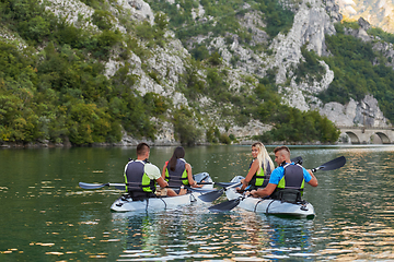 Image showing A group of friends enjoying having fun and kayaking while exploring the calm river, surrounding forest and large natural river canyons