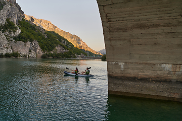 Image showing A group of friends enjoying having fun and kayaking while exploring the calm river, surrounding forest and large natural river canyons