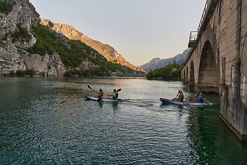 Image showing A group of friends enjoying having fun and kayaking while exploring the calm river, surrounding forest and large natural river canyons