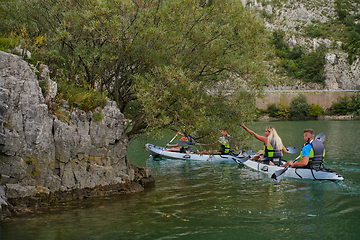 Image showing A group of friends enjoying having fun and kayaking while exploring the calm river, surrounding forest and large natural river canyons