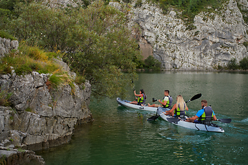 Image showing A group of friends enjoying having fun and kayaking while exploring the calm river, surrounding forest and large natural river canyons