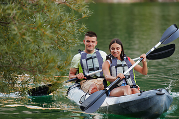 Image showing A young couple enjoying an idyllic kayak ride in the middle of a beautiful river surrounded by forest greenery