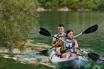 Image showing A young couple enjoying an idyllic kayak ride in the middle of a beautiful river surrounded by forest greenery