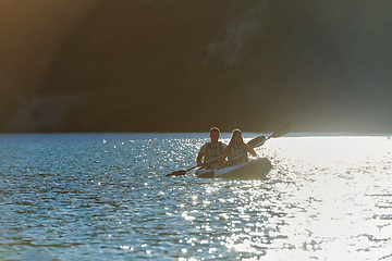 Image showing A young couple enjoying an idyllic kayak ride in the middle of a beautiful river surrounded by forest greenery in sunset time