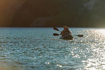 Image showing A young couple enjoying an idyllic kayak ride in the middle of a beautiful river surrounded by forest greenery in sunset time