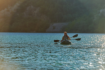 Image showing A young couple enjoying an idyllic kayak ride in the middle of a beautiful river surrounded by forest greenery in sunset time