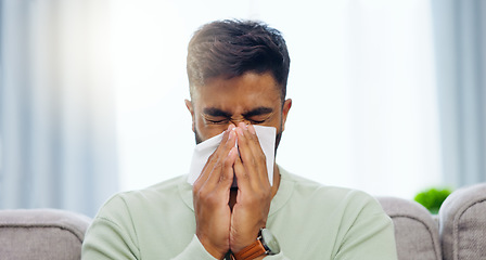 Image showing Tissue, sneeze and Indian man blowing nose on a home living room sofa feeling sick and tired. Allergy problem, virus and toilet paper of a person on a house lounge couch with sinus infection and flu