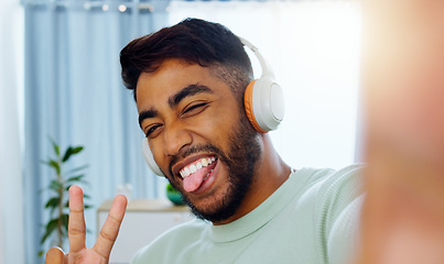 Image showing Selfie, man and smiling tongue out emoji headphones for music playlist streaming and cheerful mood in home. Wellness peace sign, audio and happy male ready to dance photograph with smile.