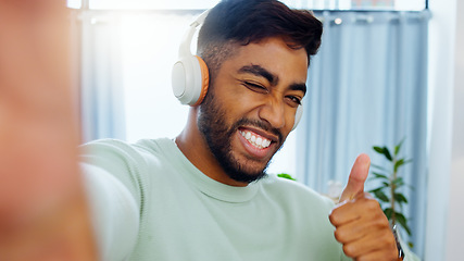 Image showing Selfie, man and smiling thumbs up emoji headphones for music playlist streaming and cheerful mood in home. Wellness peace sign, audio and happy male ready to dance photograph with smile wink