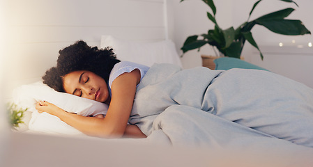 Image showing Young black woman sleeping in bed in her bedroom while resting and having a dream at home. Relax, peaceful and calm African girl taking a nap with a comfortable pillow and blanket at her house.