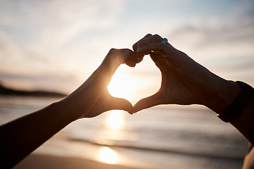 Image showing Couple, heart and hands at beach in sunset for love, care and relax on holiday, vacation and travel. Closeup of people, silhouette and finger shape at sea for support, freedom and emoji sign in sky