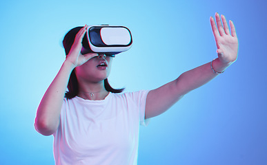 Image showing Metaverse, headset and a woman on a blue background, touching for experience and VR gaming. Virtual reality, digital and a girl with glasses for a 3d online game or entertainment on a studio backdrop